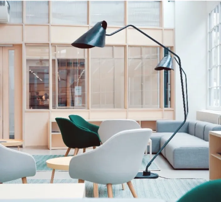 A black adjustable floor lamp arching over a bright lounge with white and green chairs, a low wooden table and a gray sofa.